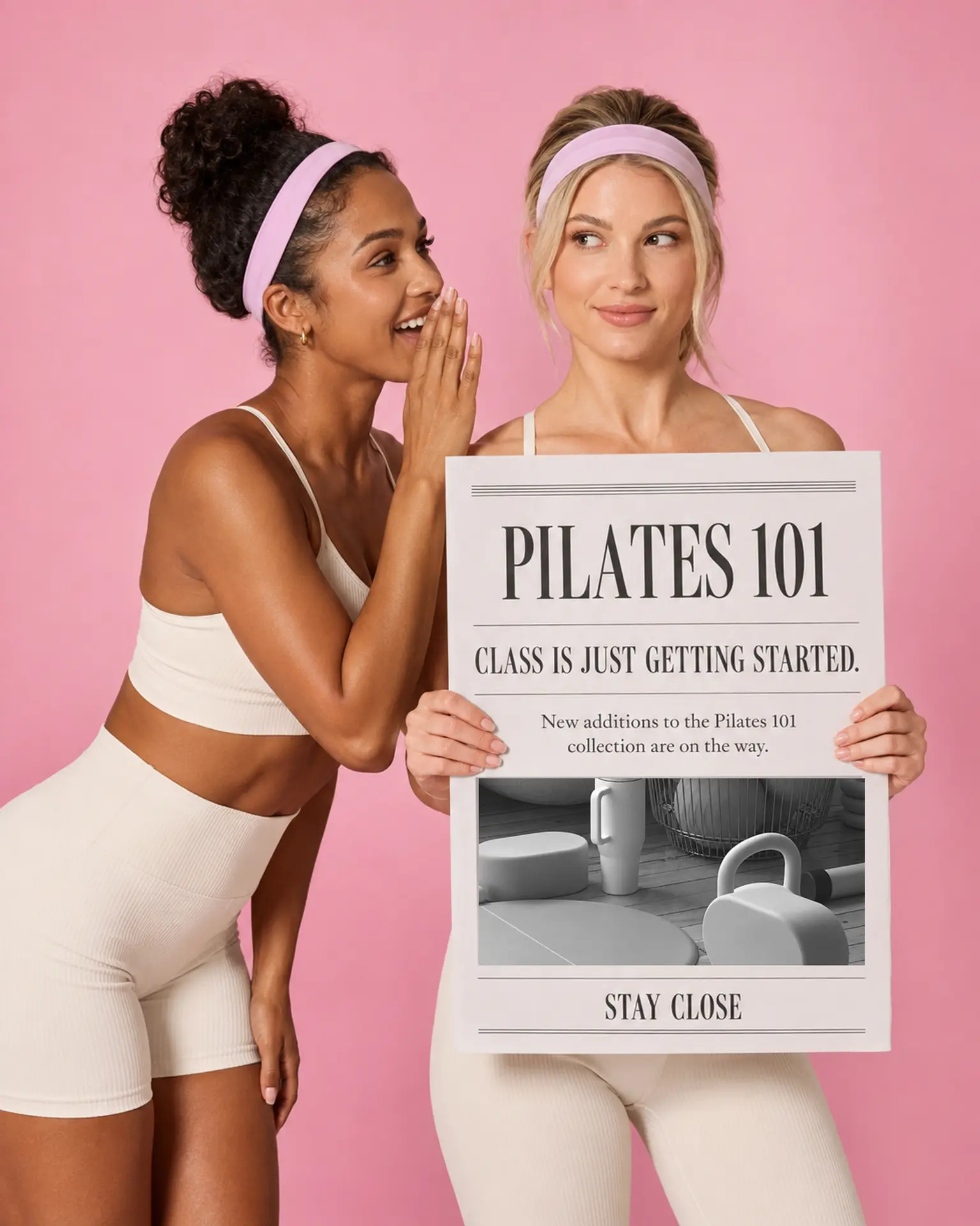 Two women in ivory workout sets holding a Pilates 101 newspaper against a pink background
